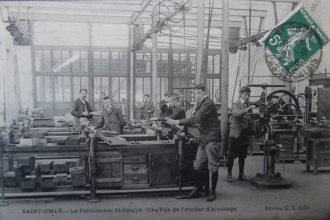 Les éléves pouvaient apprendre à se servir des machines et réaliser des travaux de mécanique générale. On peut voir les courroies qui entraînaient ces machines. Et au premier plan des éleves qui se servent d'une lime. On voit dans le fond le professeur.